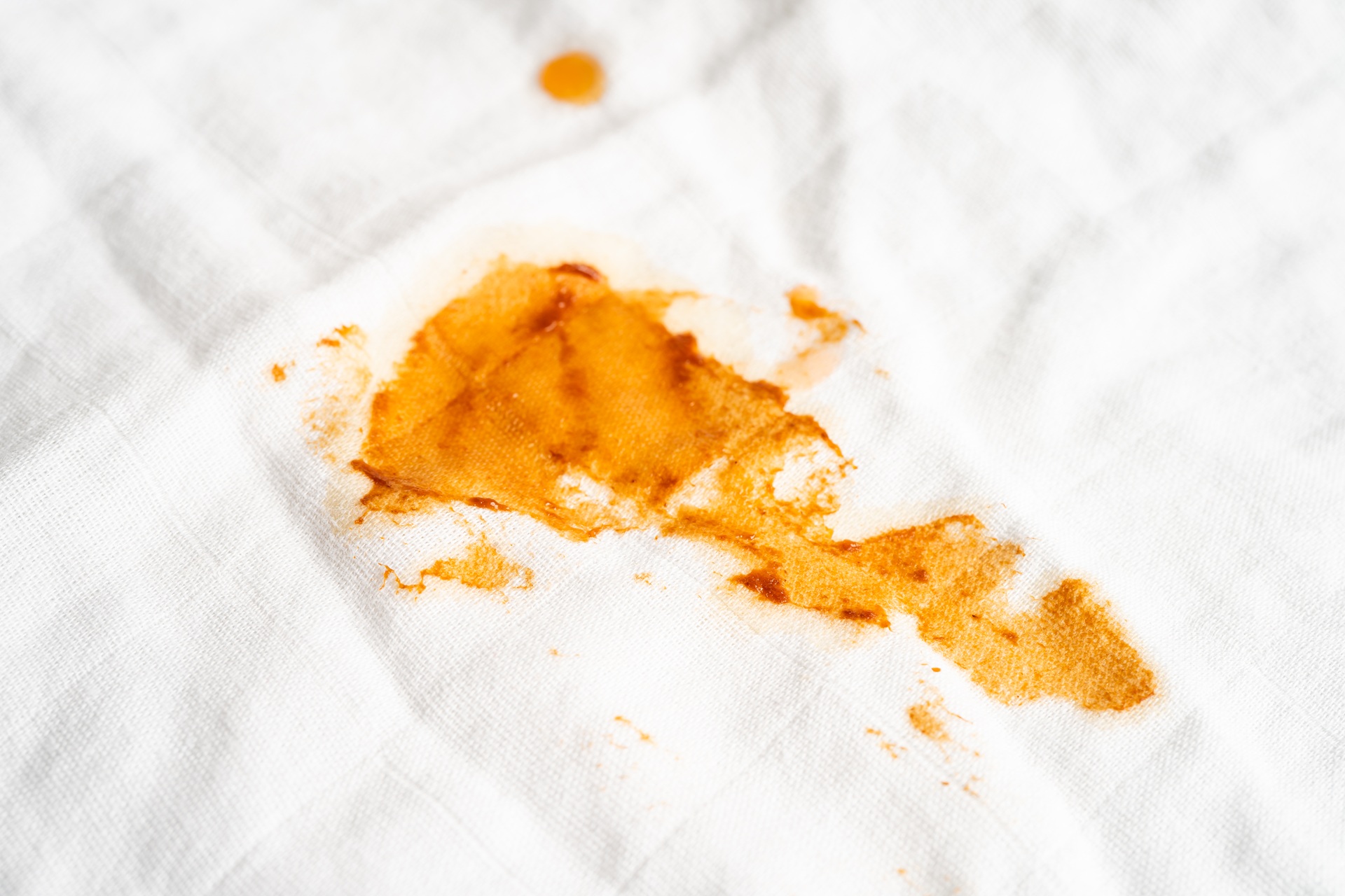 A close-up of an orange-brown sauce or oil stain on a white fabric surface.