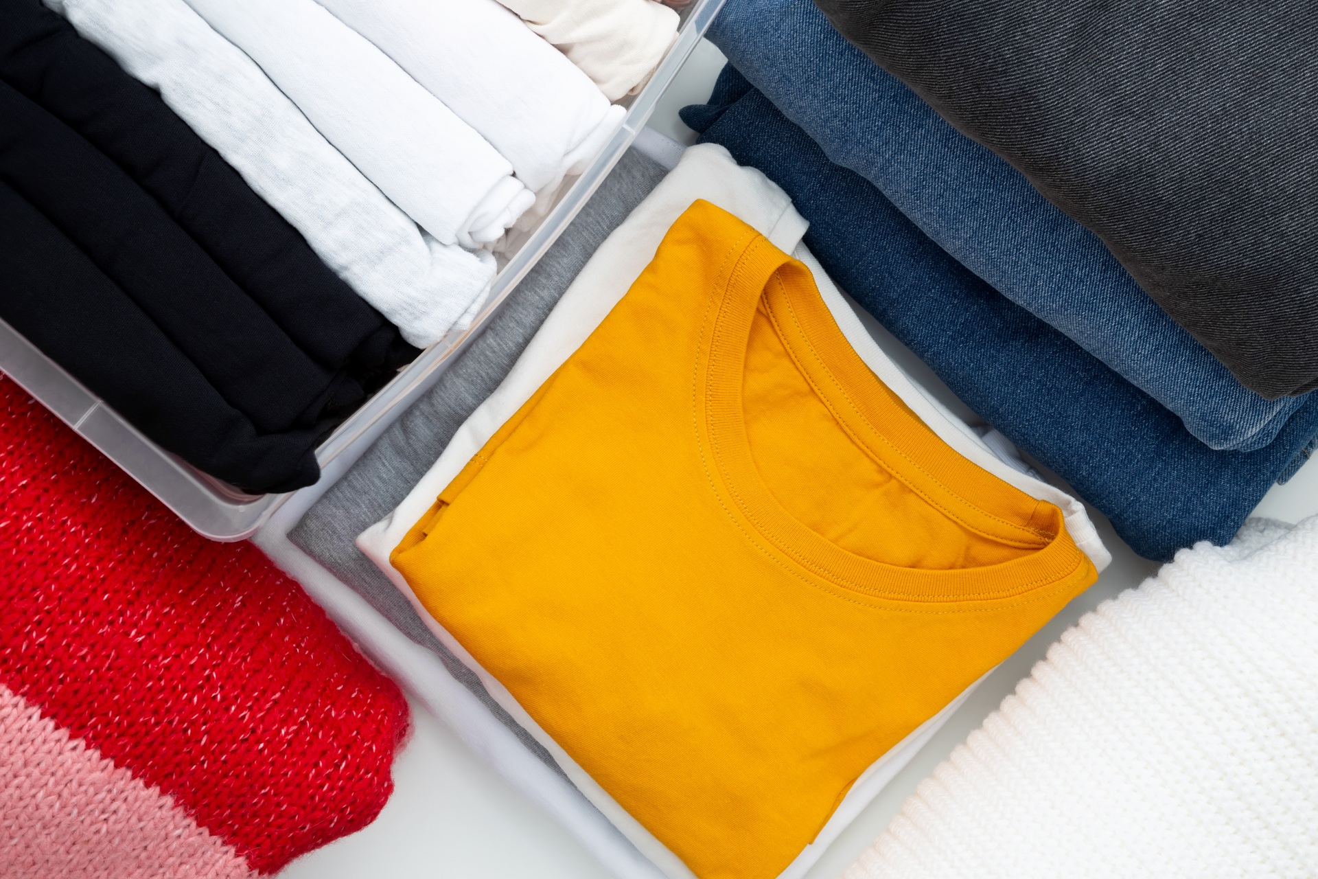Assorted folded clothes in storage bins, featuring a prominent yellow shirt, illustrating the process of refreshing stored garments for spring.