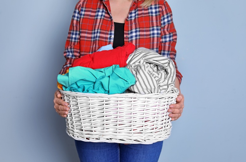 Person holding a white wicker basket filled with colorful laundry, representing convenient laundry services and garment care by Sunny Cleaners.