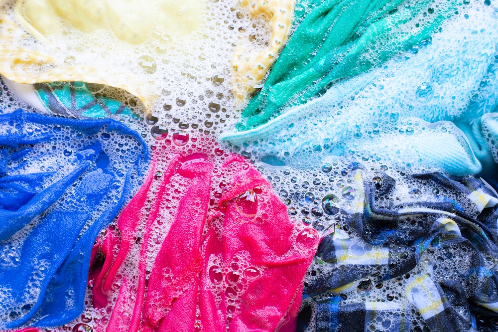 Colorful laundry items submerged in soapy water, illustrating the importance of separating whites and colors to prevent dye bleeding during washing.